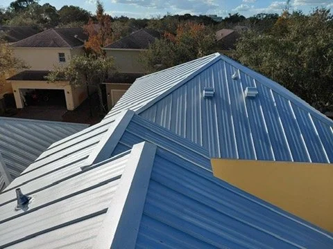 Close-up view of a metal roof with overlapping panels, part of a residential building, with trees and houses in the background.