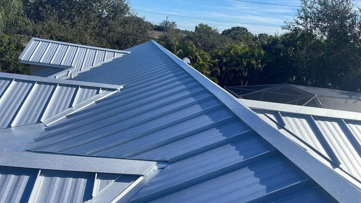 View of multiple newly installed metal roofs on a building, with a background of trees and a clear sky.