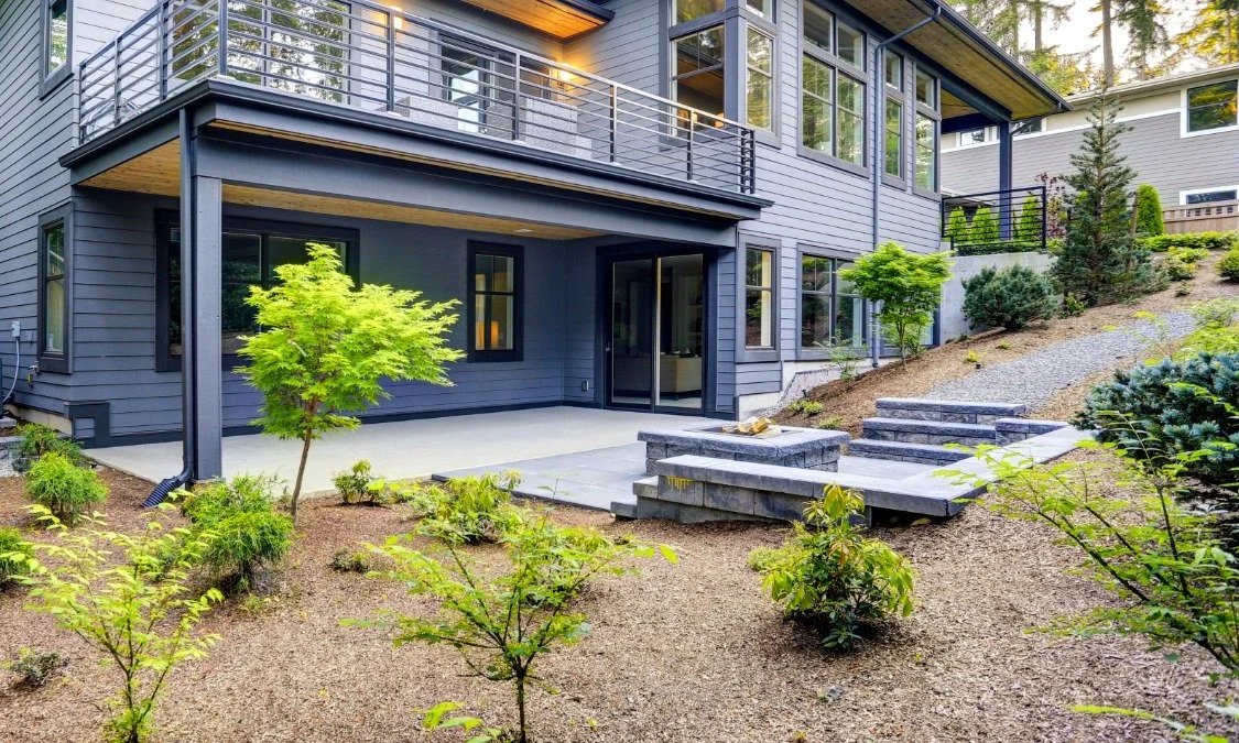 Home with a terrace, custom-built stone fire pit area, and trees for a backyard landscape design in Bend Oregon