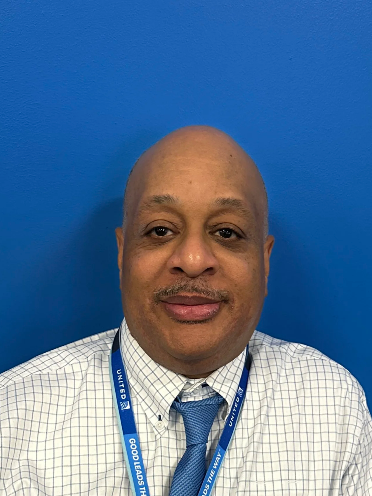 Professional headshot of a man in a suit and tie, with a serious expression and a blurred blue background.