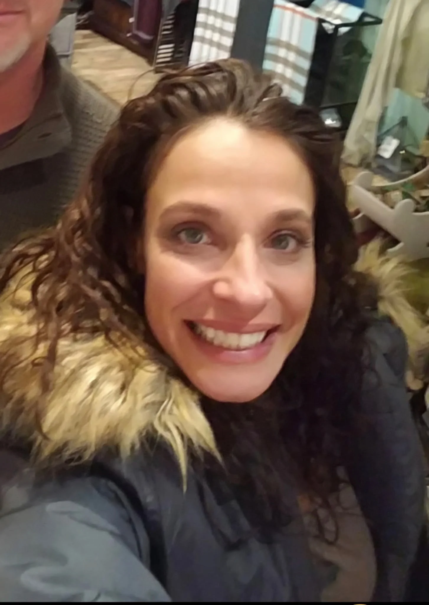 Businesswoman with curly brown hair, wearing a black blazer and white blouse, smiling at the camera.