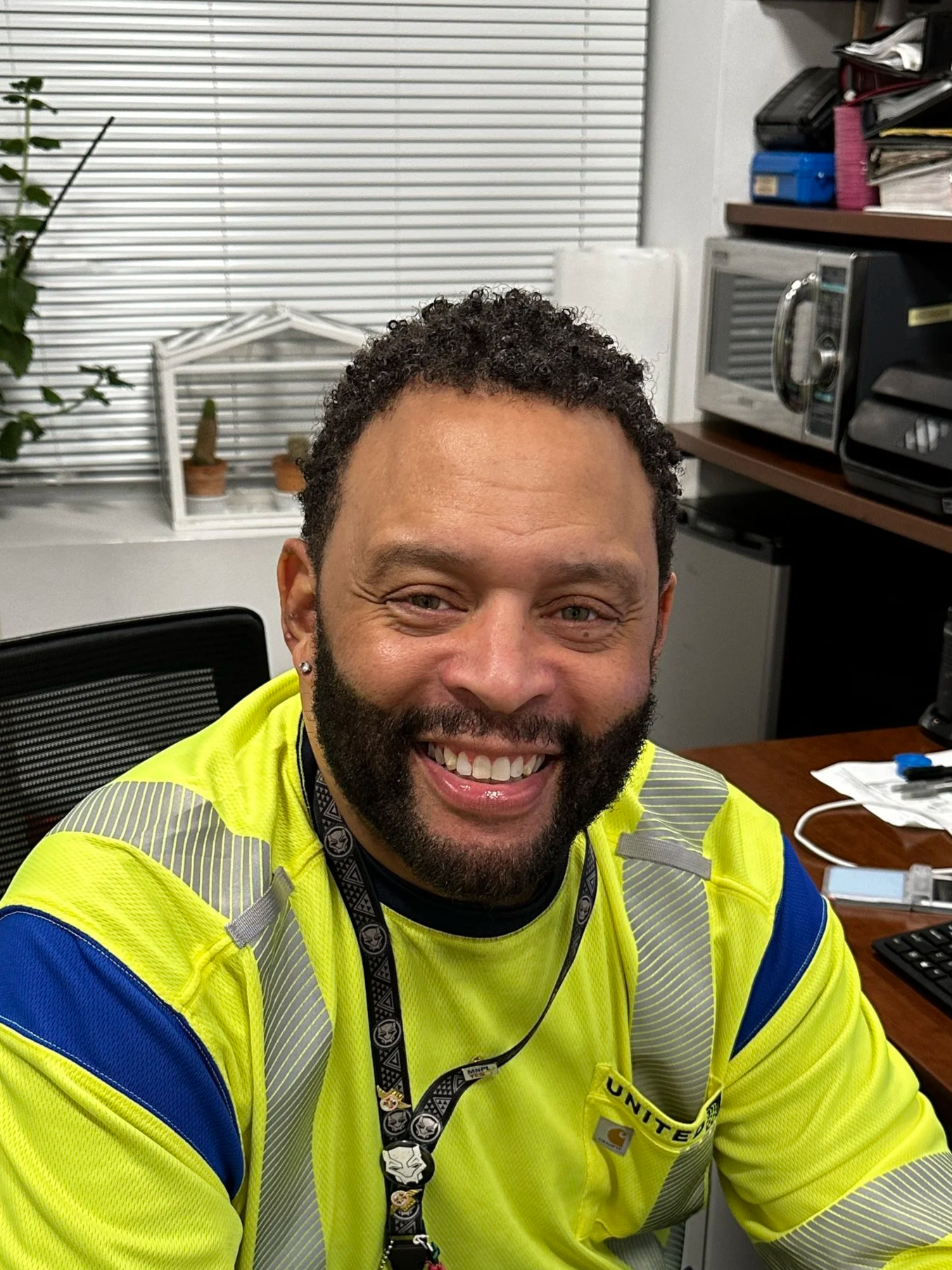 Headshot of a smiling African American man in a light gray suit, light blue shirt, and dark blue tie against a dark background.