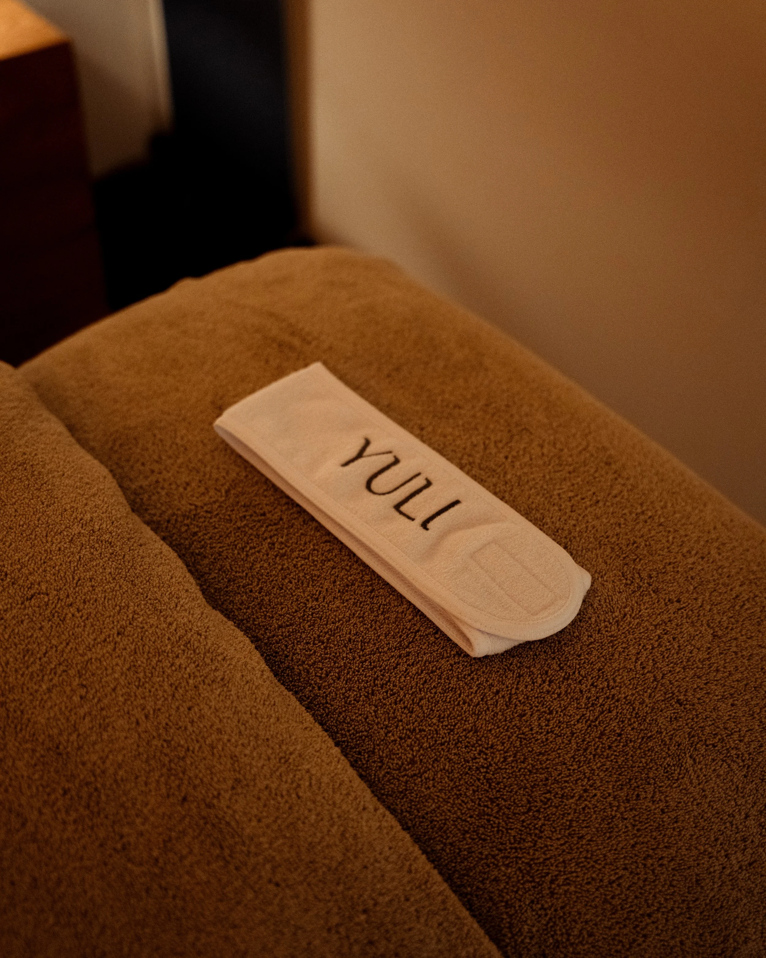 A folded white towel with the word 'YULI' written on it in black letters, placed on a beige upholstered armchair.