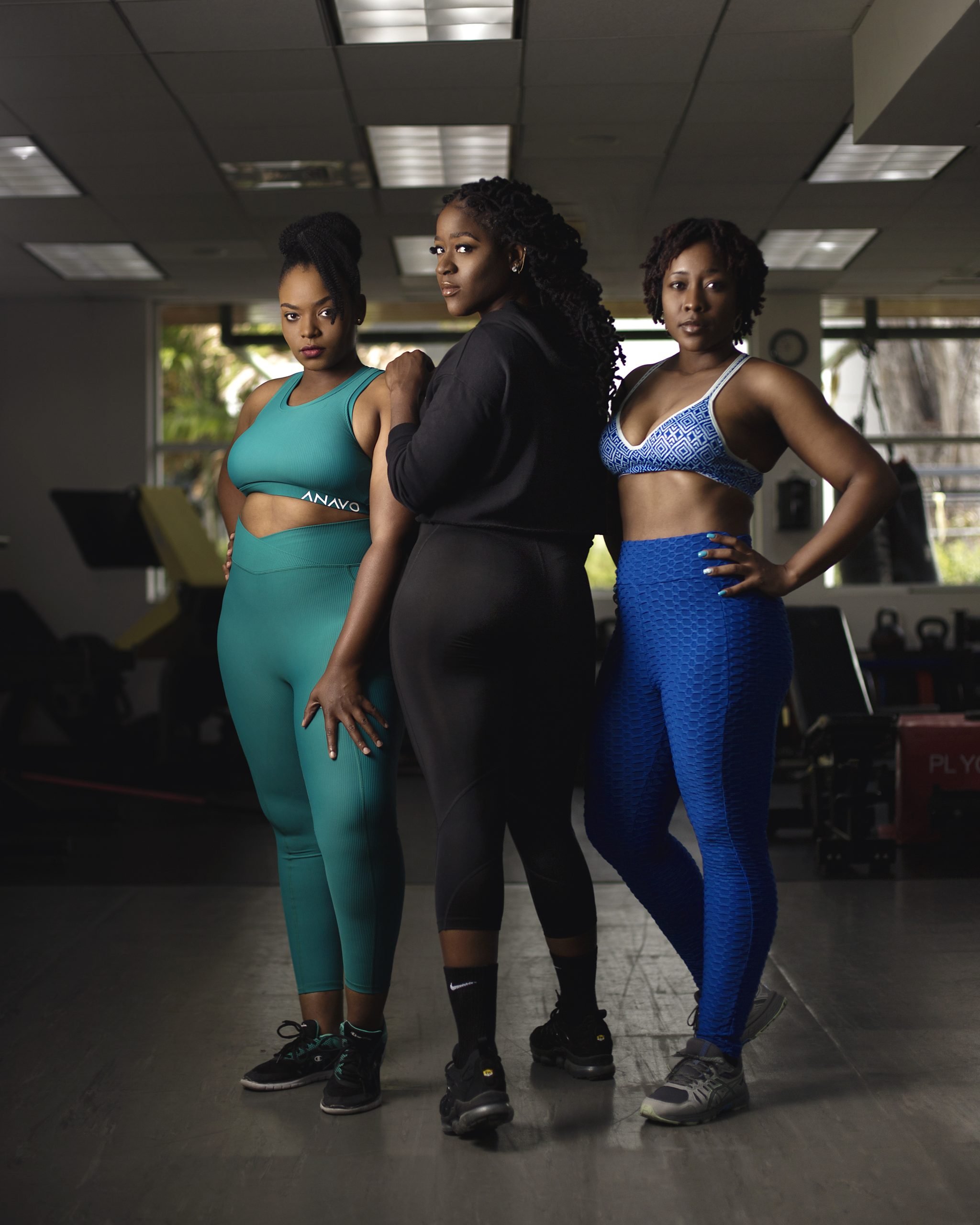 Three women in athletic wear standing in a gym, posing confidently for the camera.