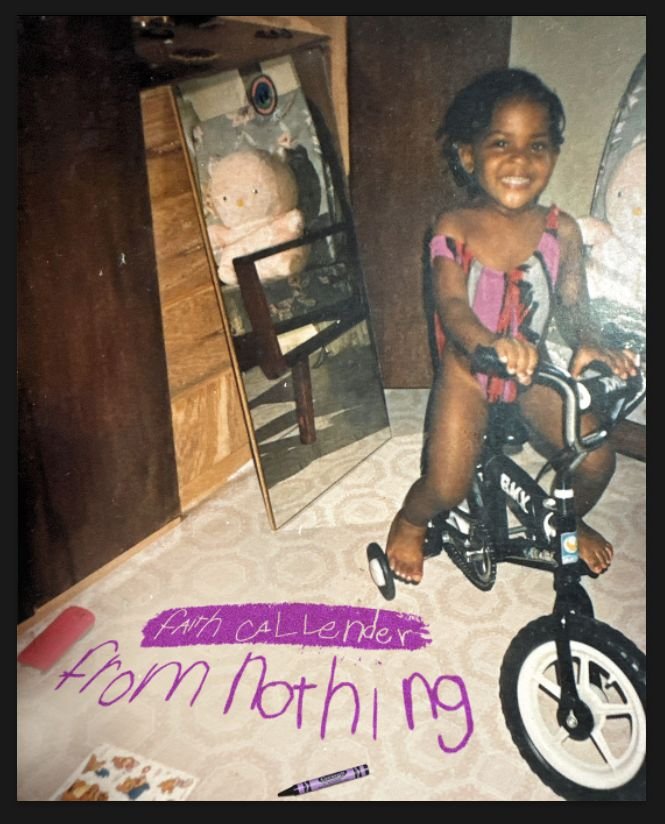 A young girl with dark curly hair smiling while sitting on a small black bicycle inside a room. There is a large mirror leaning against the wall reflecting a stuffed animal, possibly a bear, and a wooden chair. On the floor, there is a piece of purple paper with handwritten messages, one reading 'Earth called me from nothing' in purple marker. A crayon and a small piece of paper with images are also on the floor.