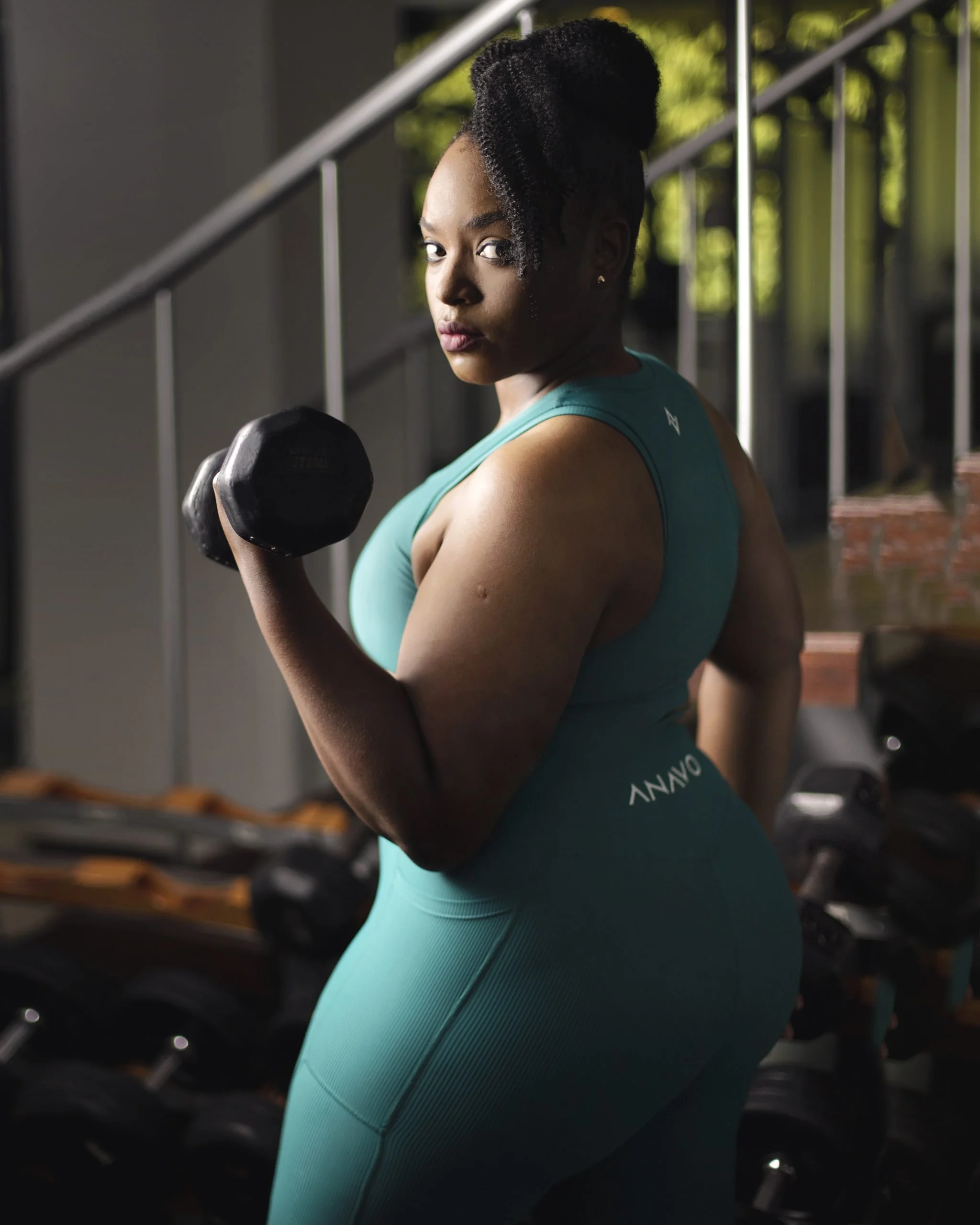 A woman in teal workout attire holding a dumbbell in a gym.