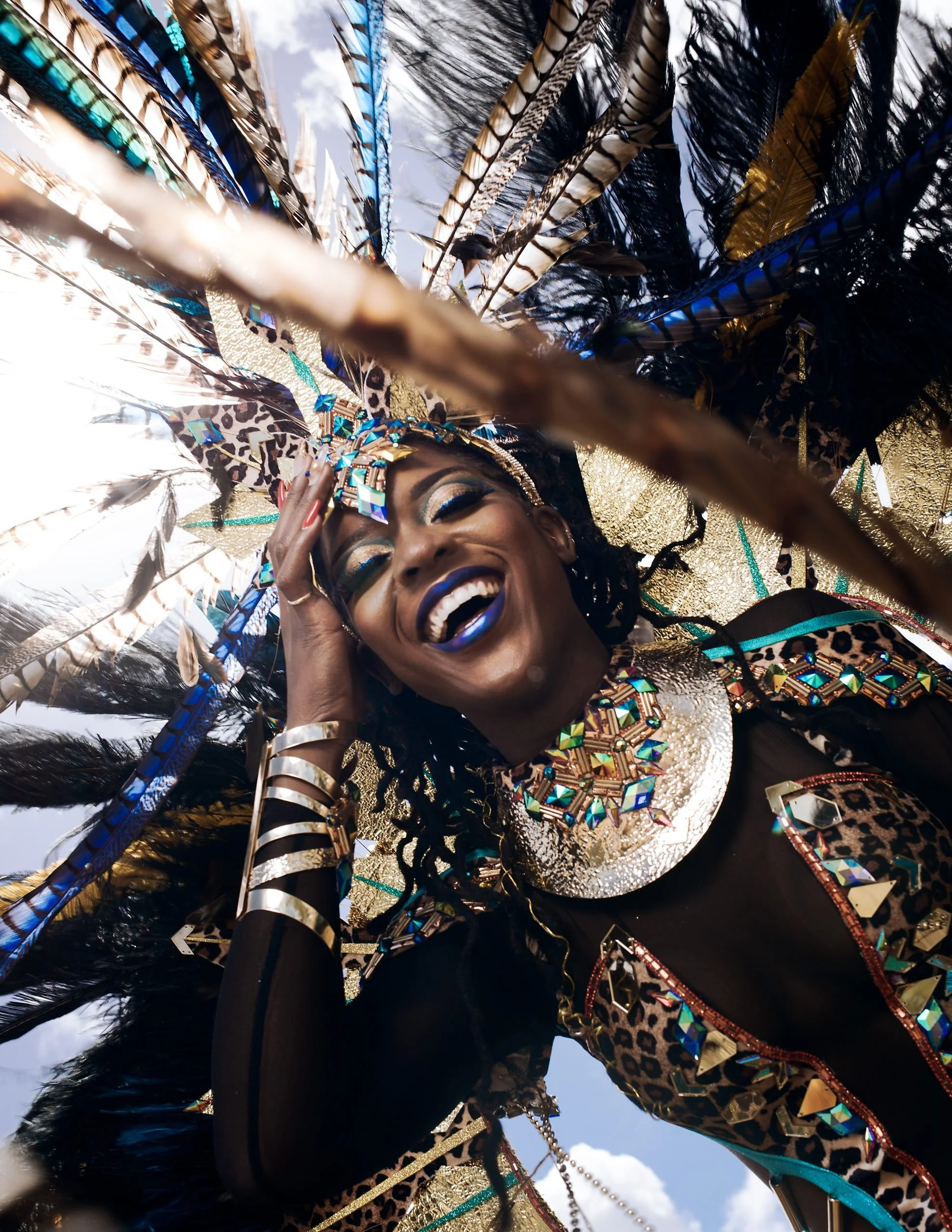 Faith Callender posing in a carnival costume with feathers, jewelry, and face paint, smiling joyfully.