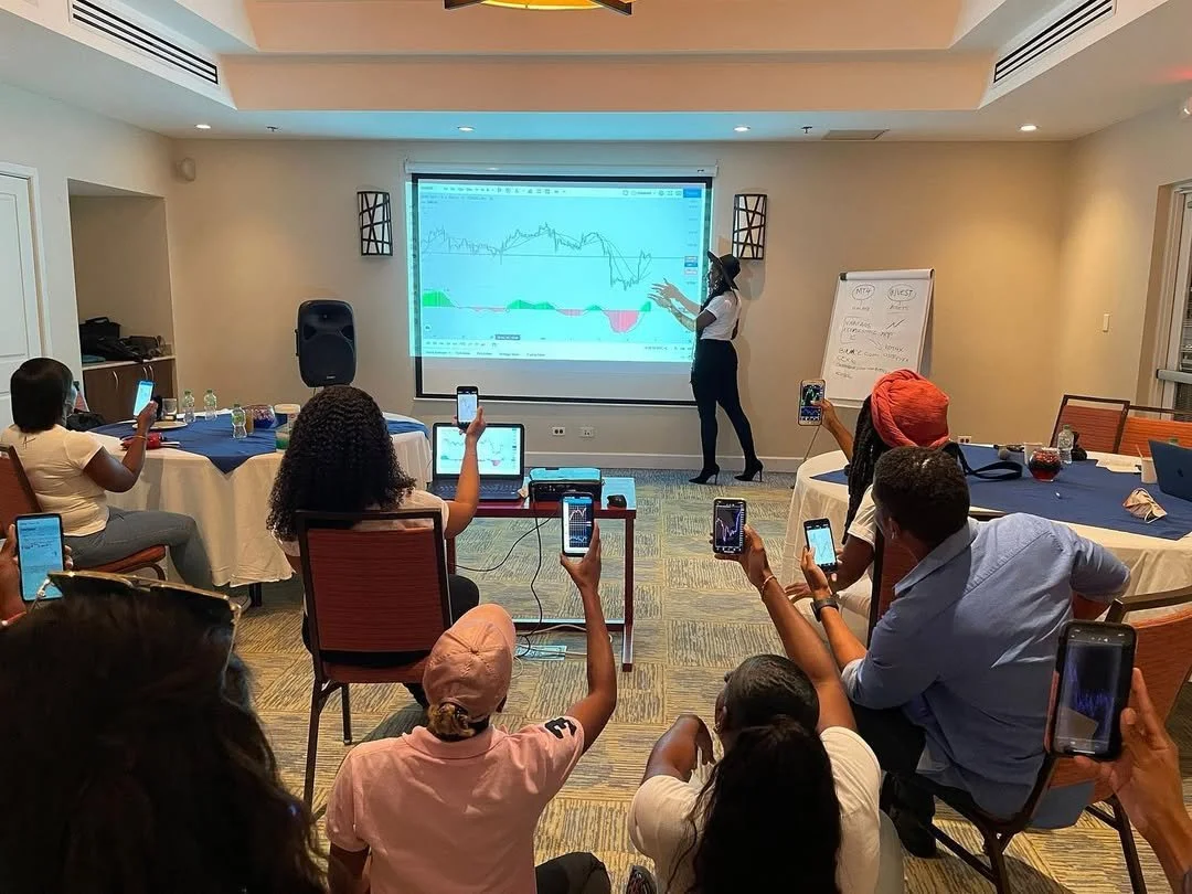 A woman gives a presentation to a group of people in a conference room with a screen displaying a financial chart, and some attendees are taking photos with their smartphones.