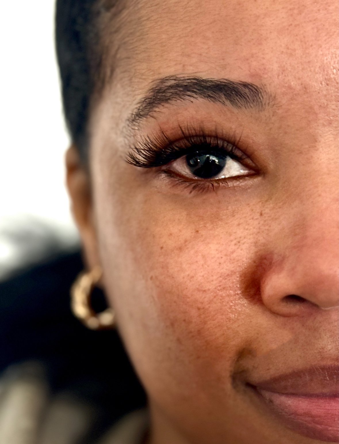 Close-up of a woman's face, showing her eye, part of her cheek, and a smile, with a hoop earring in her ear.
