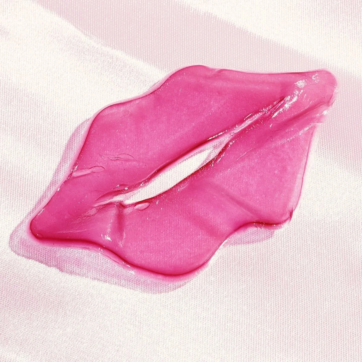 Close-up of pink lipstick smudged on a white fabric background.