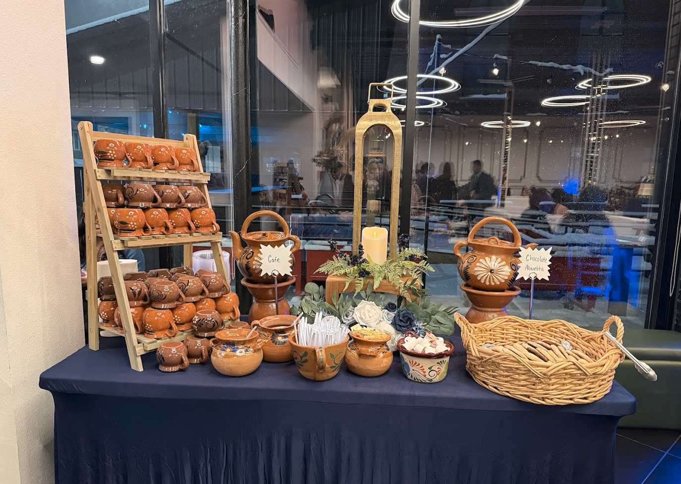 Display of small, brown, decorative ceramic teapots arranged on a shelving unit, along with bowls, a basket, candles, and decorative items on a table at a festive event.
