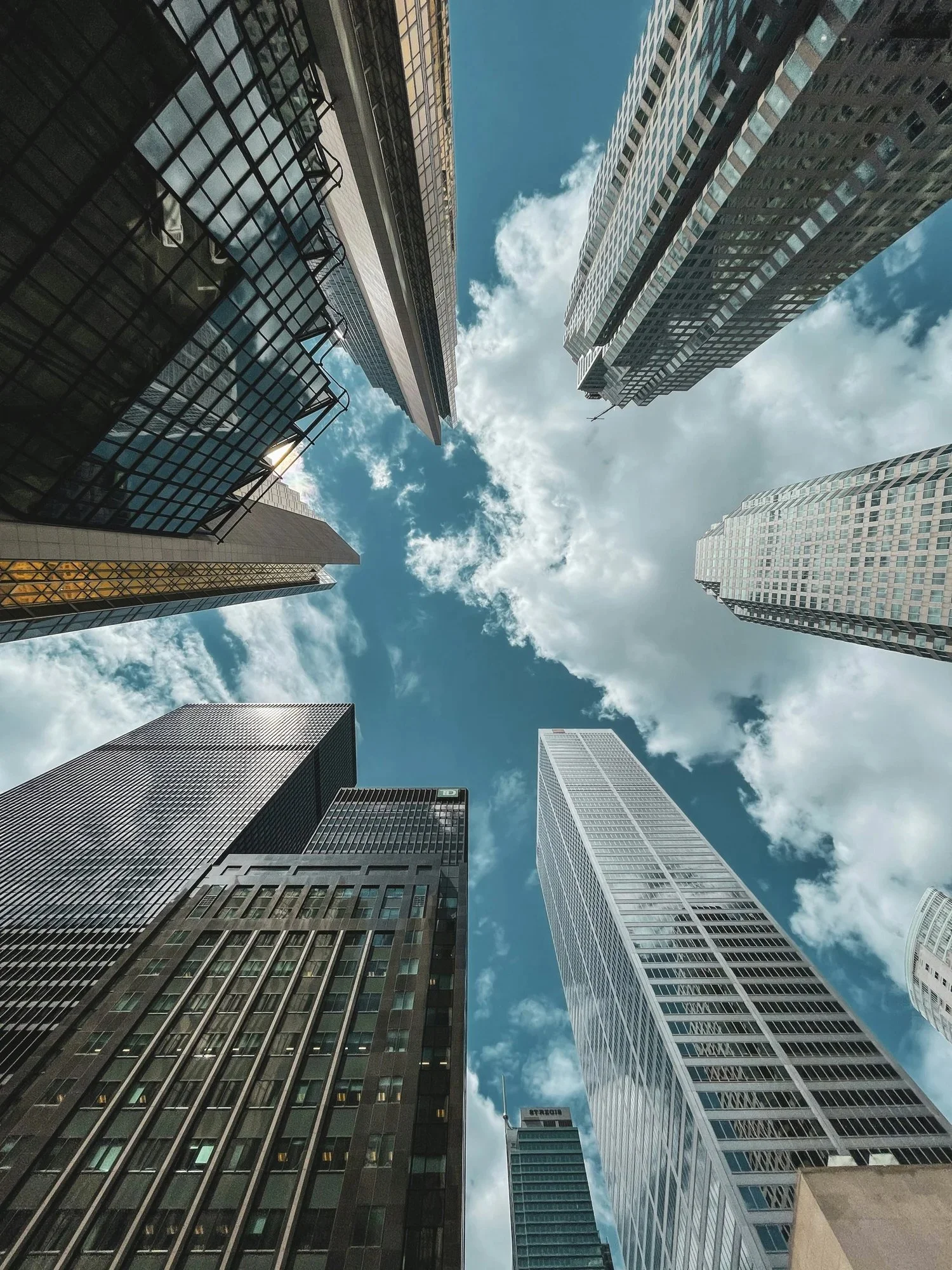 Looking up at tall modern skyscrapers in a city with a partly cloudy sky.