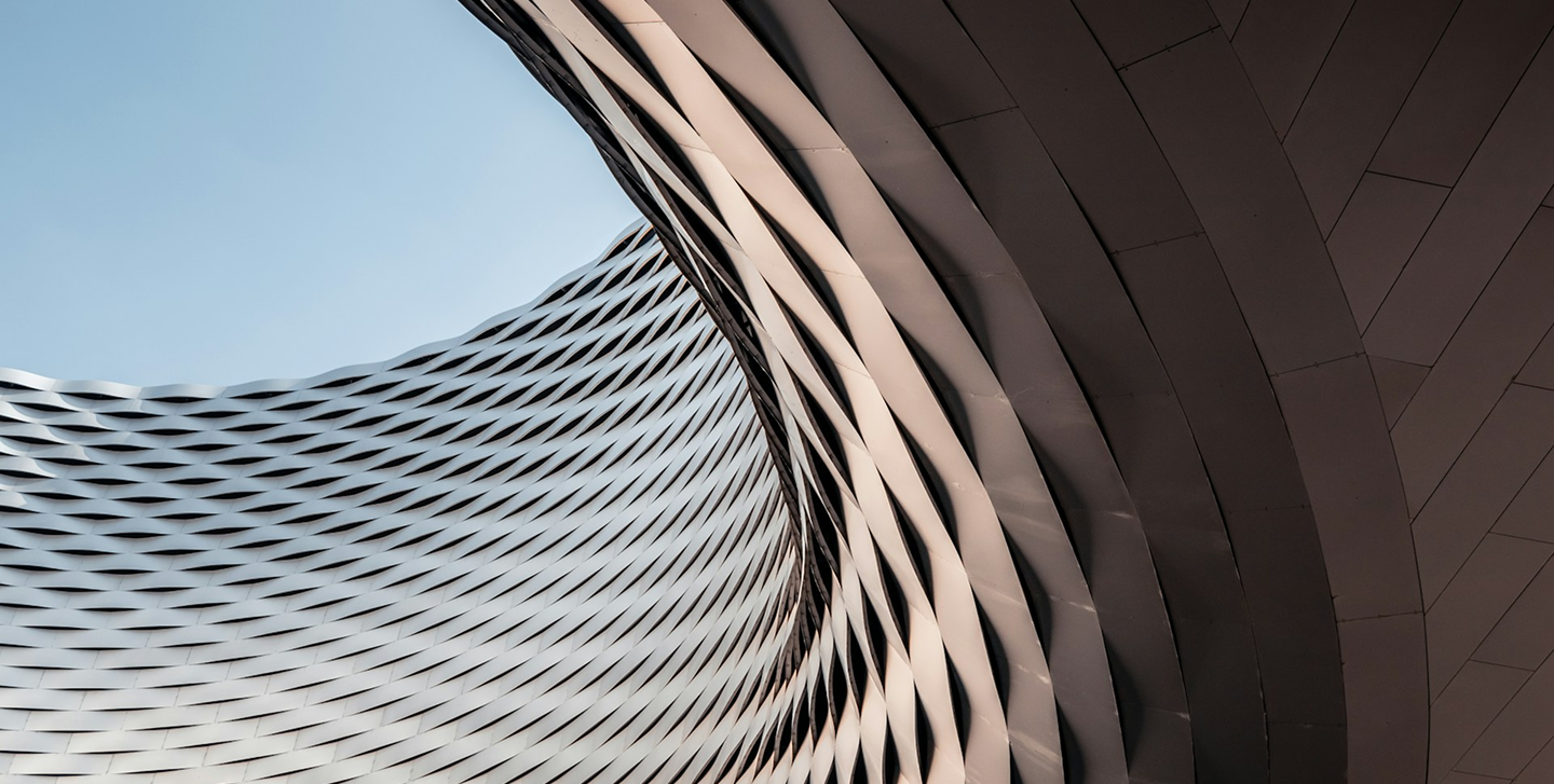 Close-up of modern, curved architectural building with metal panels and intricate diamond-shaped pattern.