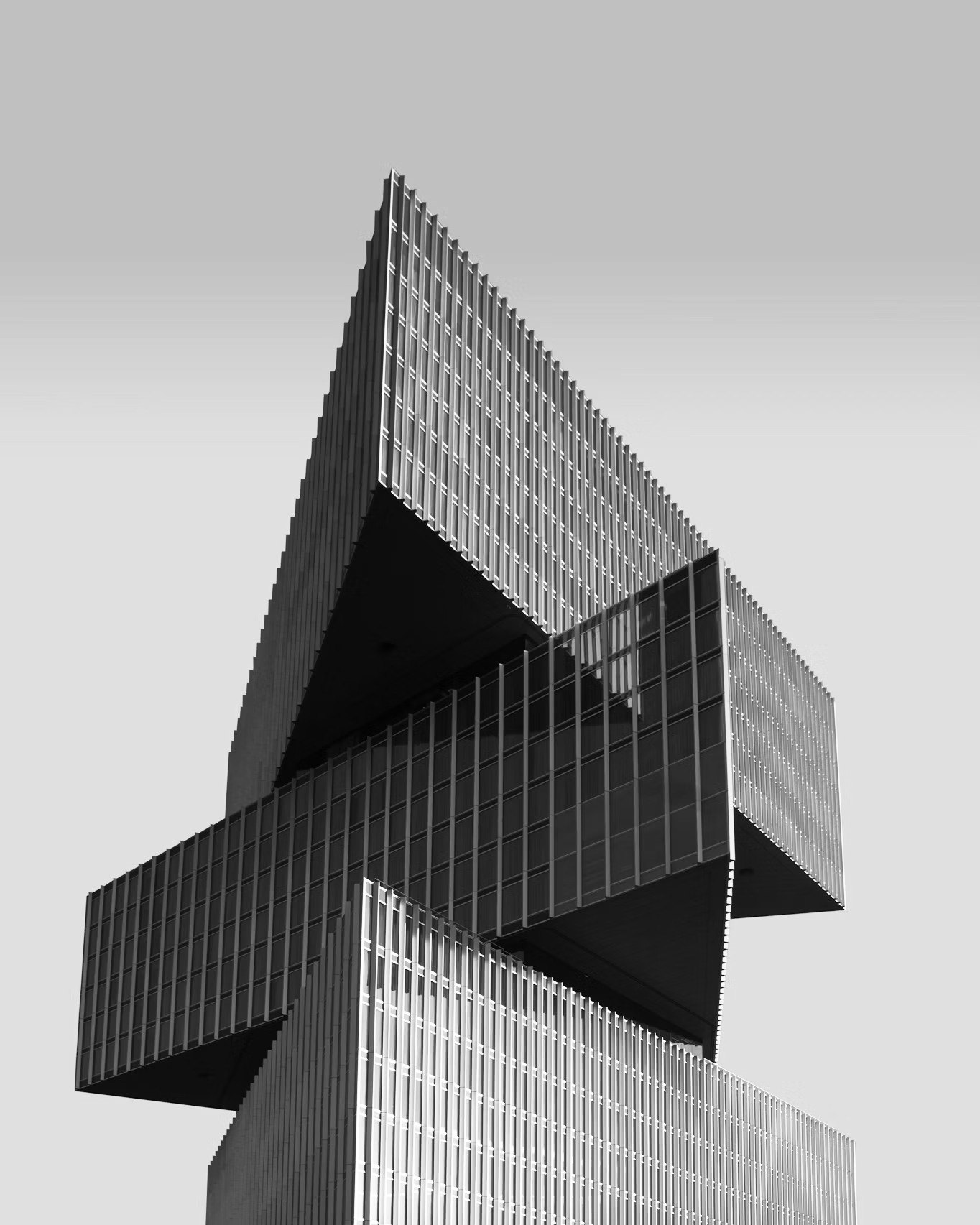 A modern skyscraper with multiple stacked and cantilevered sections, featuring glass windows and vertical lines, against a cloudy sky.