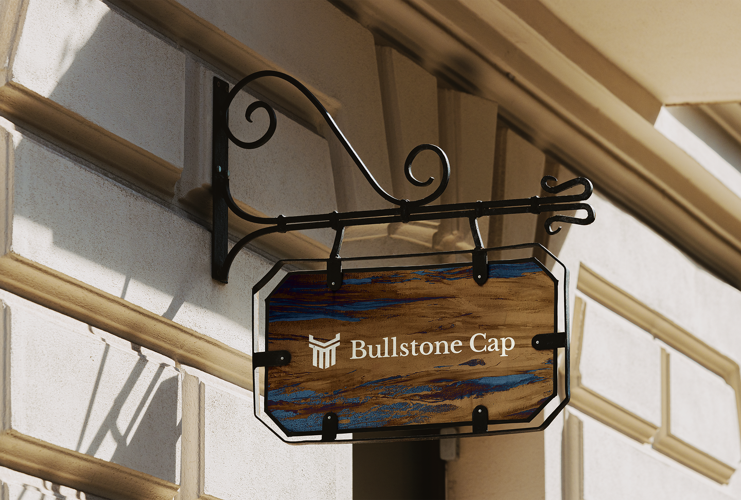 Storefront sign with the text "Bullstone Cap" and a logo, hanging on a beige building with decorative trim.
