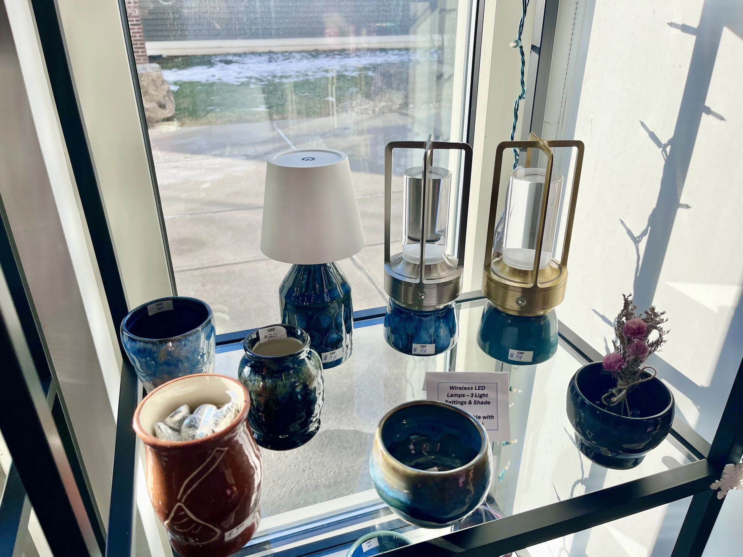 Display of ceramic planters and lamps near a glass window, with a sign that reads 'Wireless LED Lamps - 3 Light Cattings & Shade'.