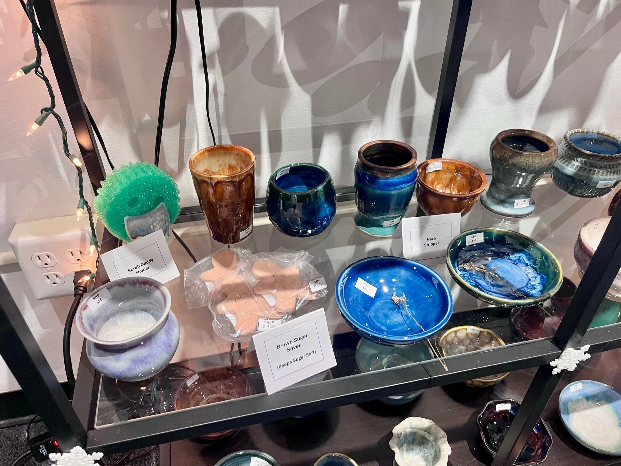 Display shelf with fused glass art bowls and cups, a green scrubbing sponge, fishing line, and small decorative plaques.