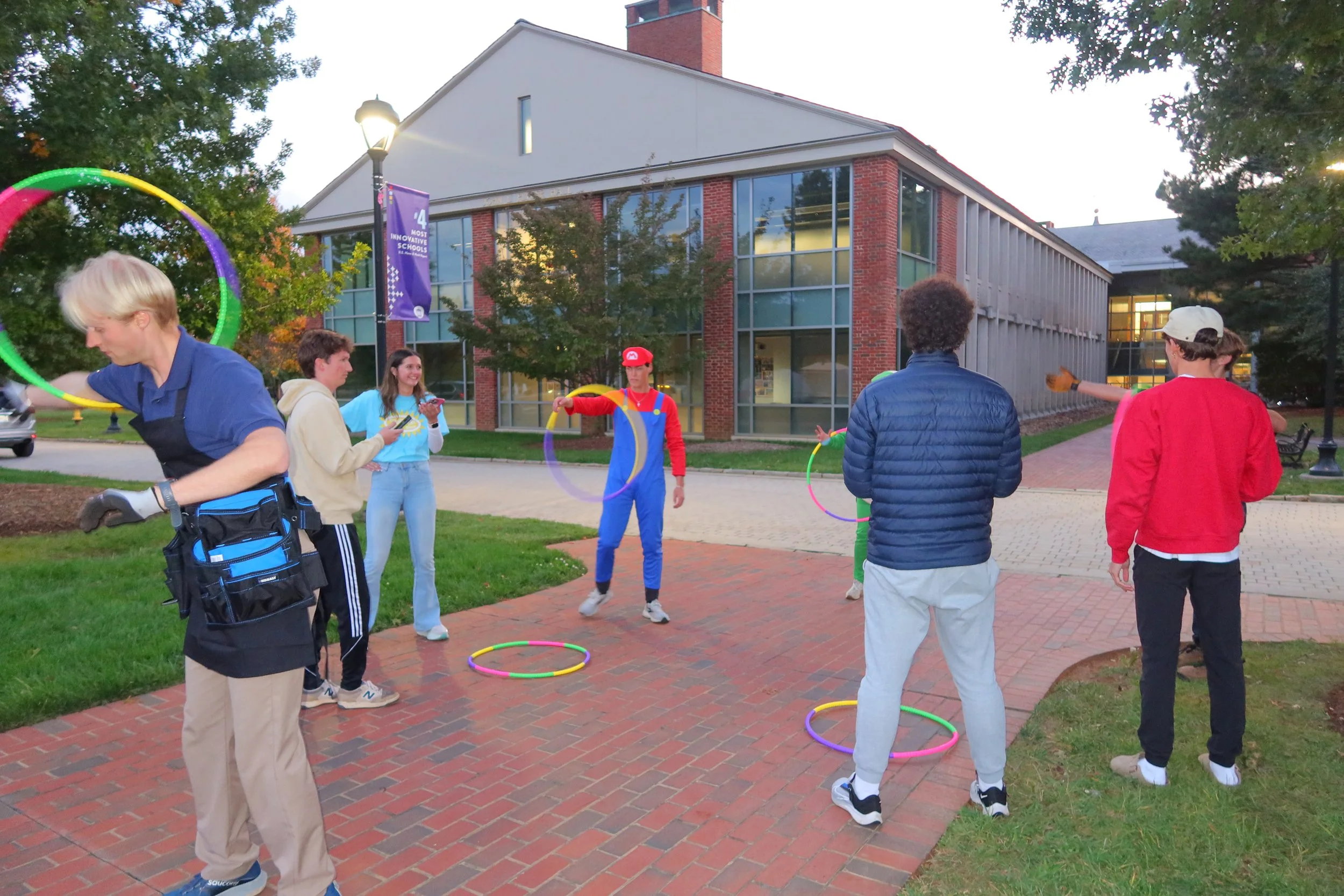 Group of people playing with hula hoops outdoors in front of a school building during the evening.
