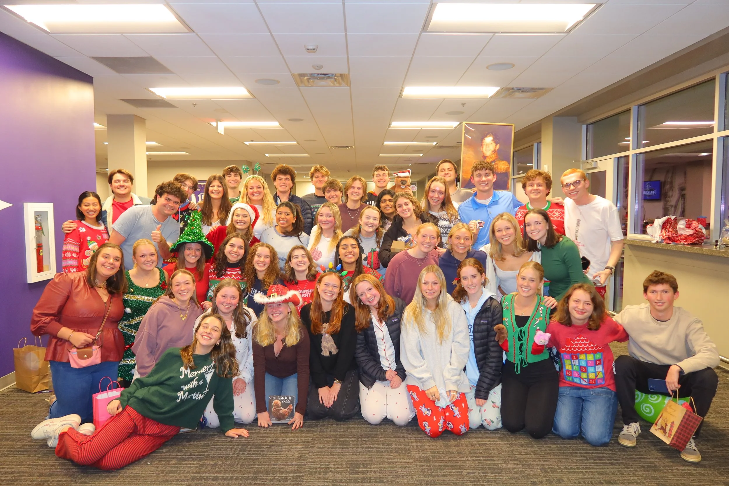 Group of young people celebrating Christmas indoors, some in festive pajamas and Santa hats, smiling for the camera.