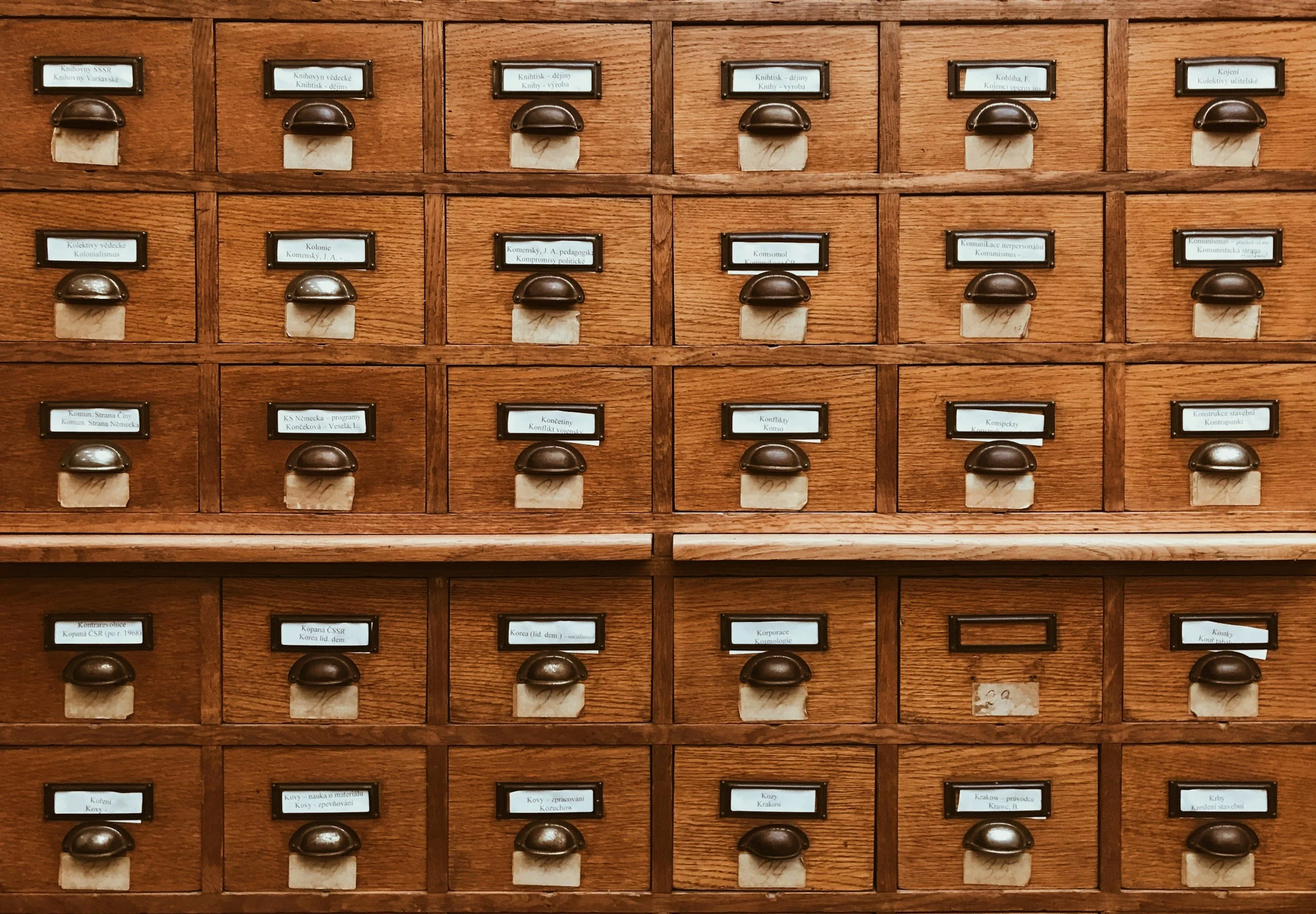 A wooden library card catalog with multiple small drawers labeled with various topics in a language that appears to be Czech or Slovak.