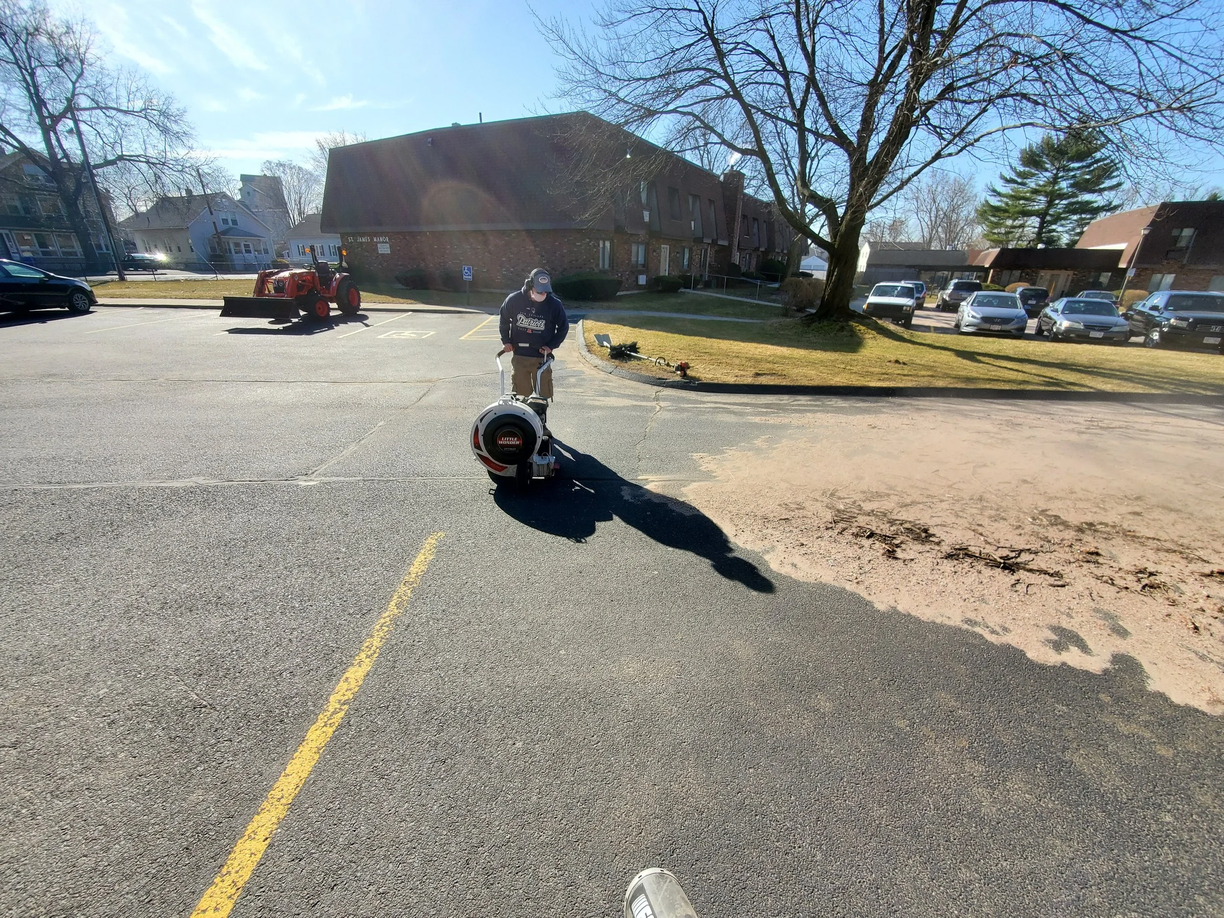 A man operating a street cleaning machine in a parking lot on a sunny day.
