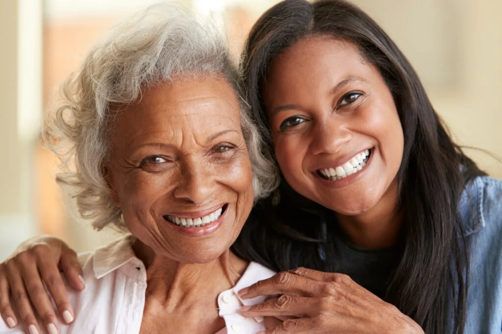 An elderly woman and a younger woman smiling and hugging.