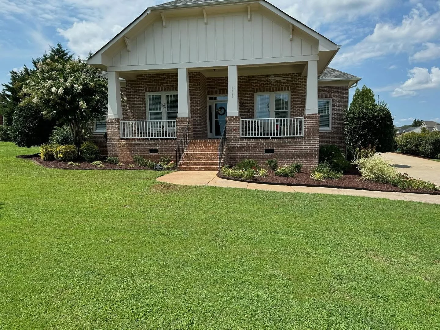 Craftsman style home with healthy green lawn and mulched garden beds with ornamental plants in front  