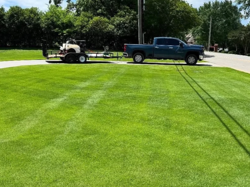 Blue pickup truck with trailer hauling lawn equipment with freshly treated green grass