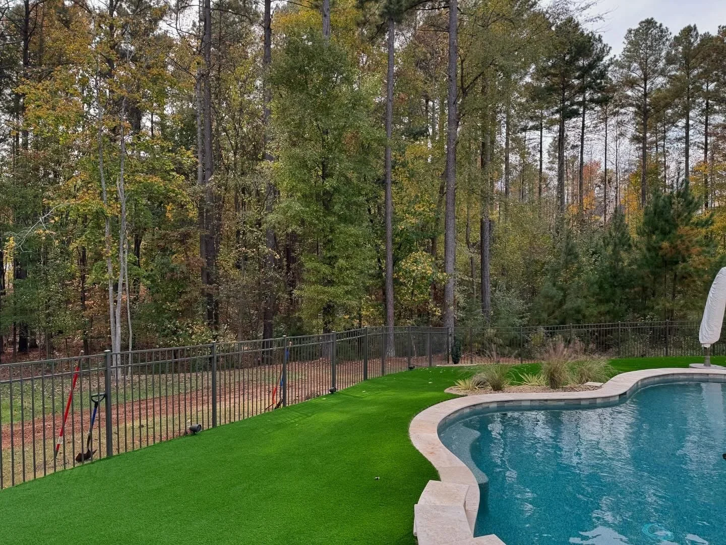 Artificial turf installed around swimming pool surrounded by trees 