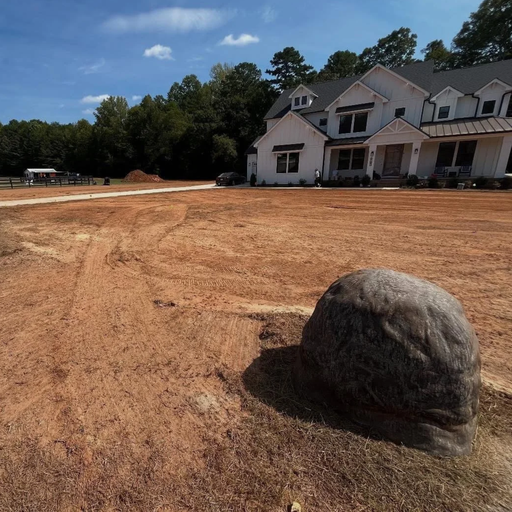 Graded dirt lawn in front of newly built white house with boulder in foreground 