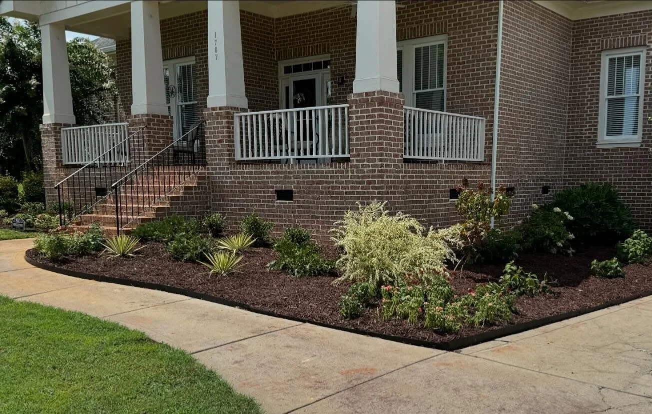 Brick house front porch with newly installed plants in a mulched garden bed