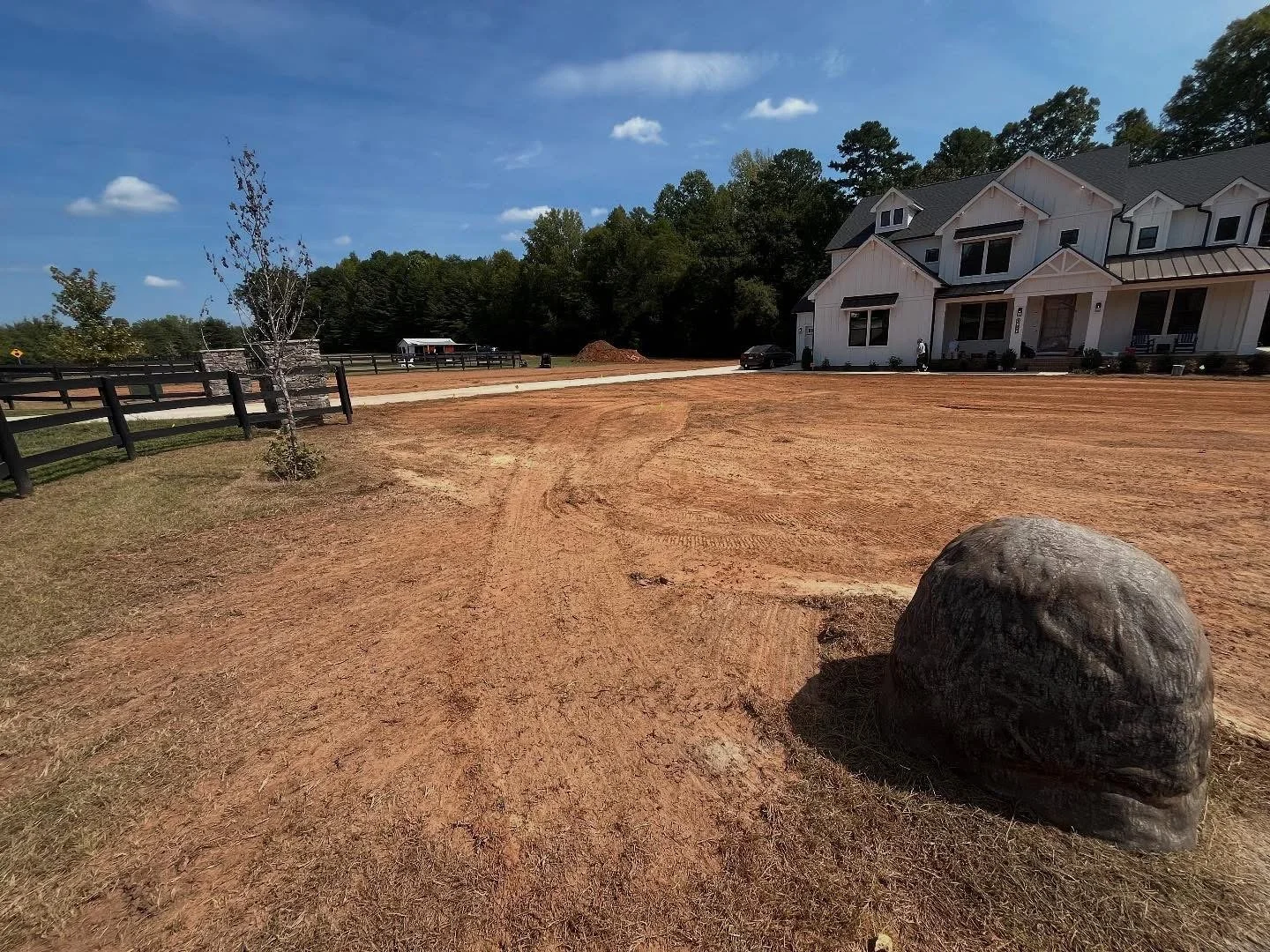 Freshly graded dirt front yard in front of a newly constructed white house with boulder 