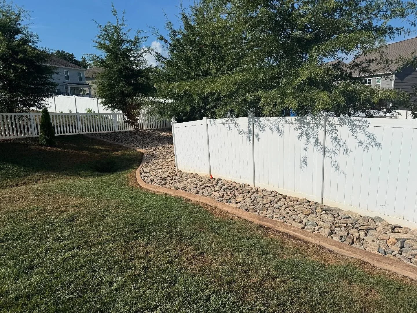 White fence with river rock and stone paver border