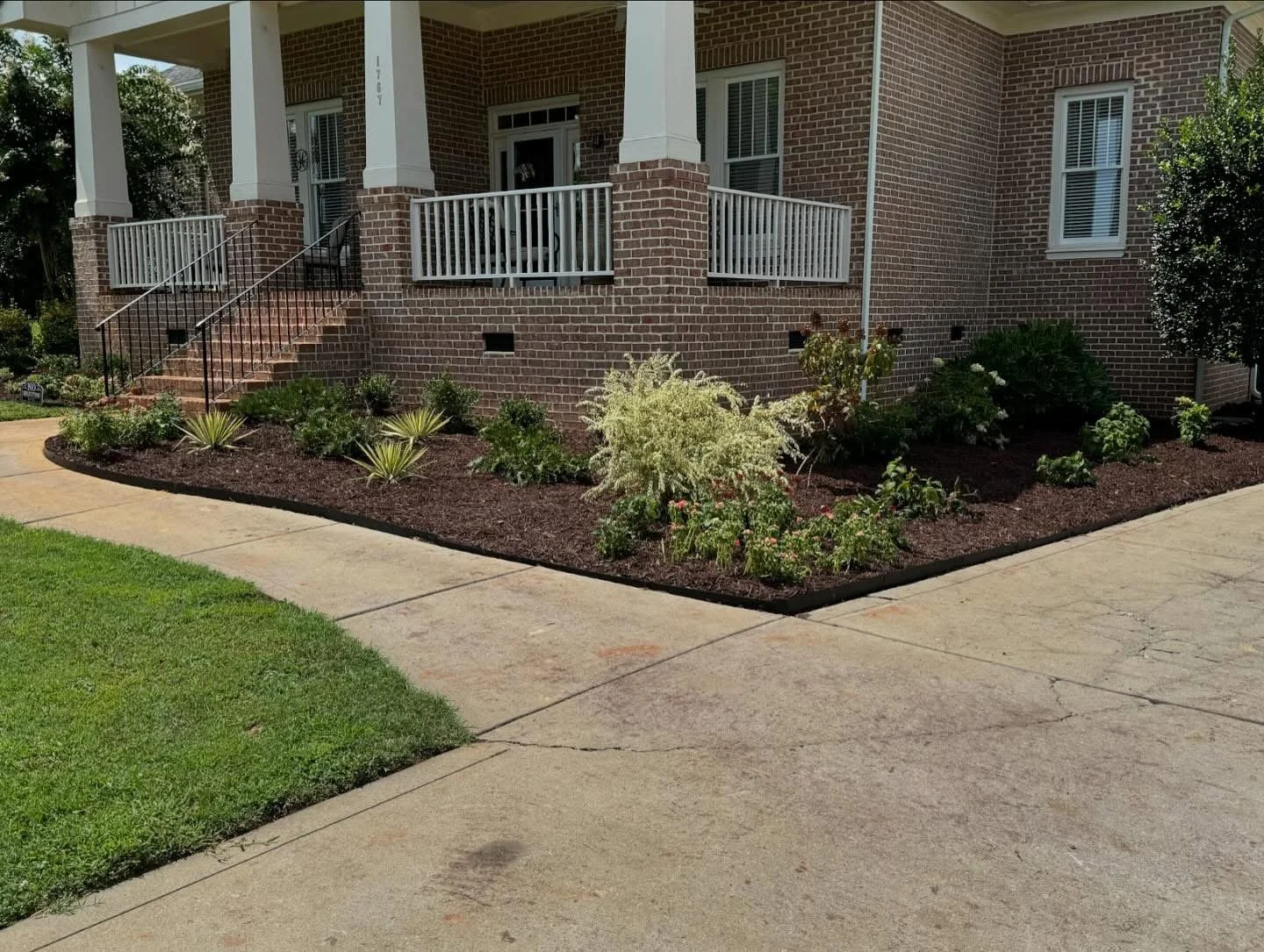 Mulched garden bed with ornamental plants in front of house 