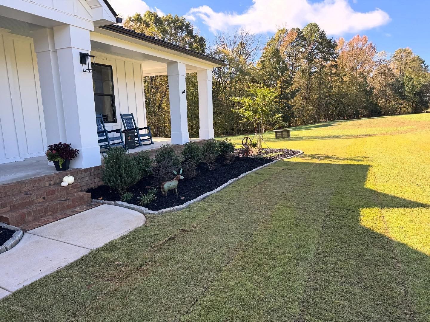 Newly laid sod and mulched garden bed with ornamental plants in front of white house 