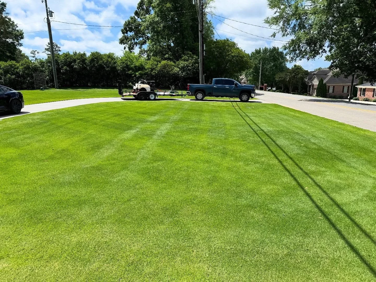 Freshly treated green lawn with blue pickup truck hauling lawn spray equipment 