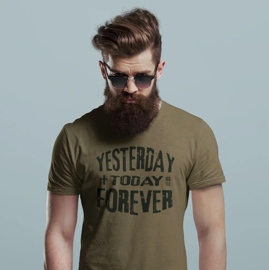 A man with a full beard and styled hair wearing round sunglasses and an olive green T-shirt with the text 'YESTERDAY + TODAY FOREVER' printed on it, standing against a plain light blue background.