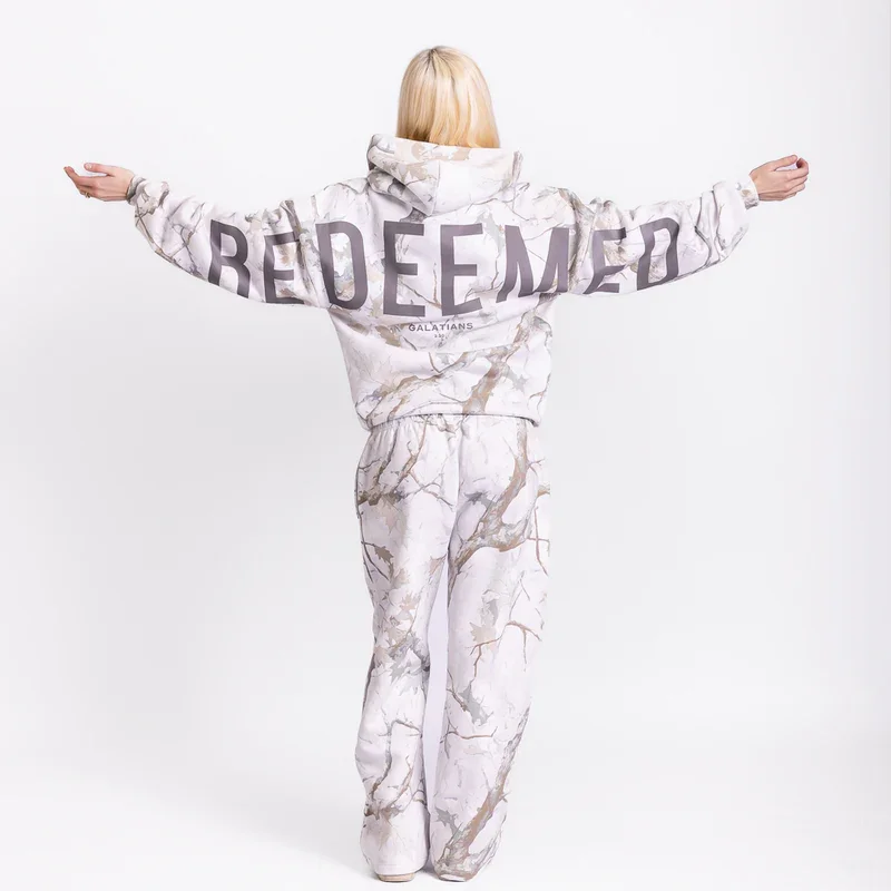 Person with blonde hair seen from behind, wearing a marble pattern hoodie and matching pants, arms extended outward, against a plain white background.