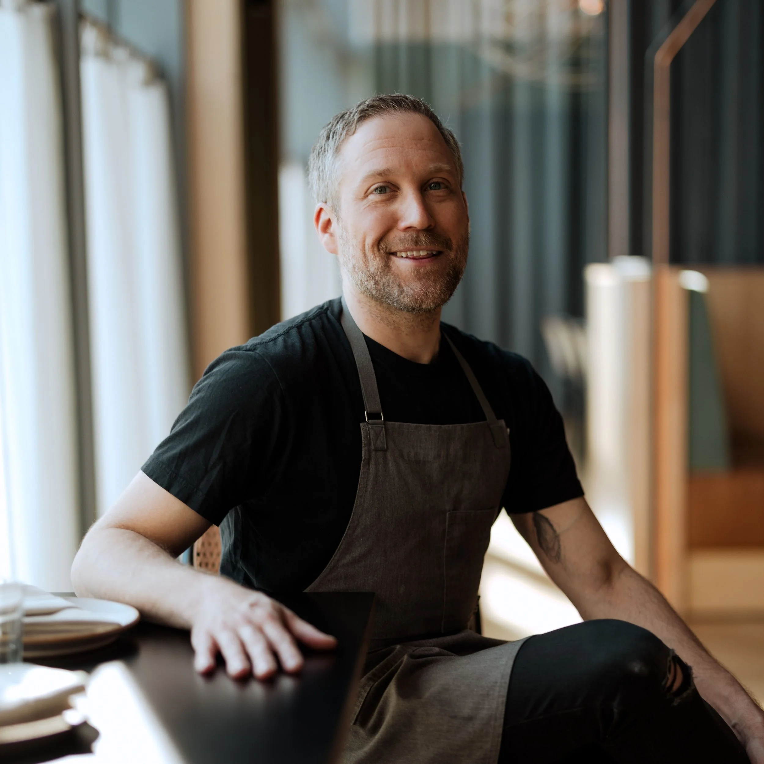 Executive Chef Johnny Spero seated in the Passage dining room wearing a chef's apron