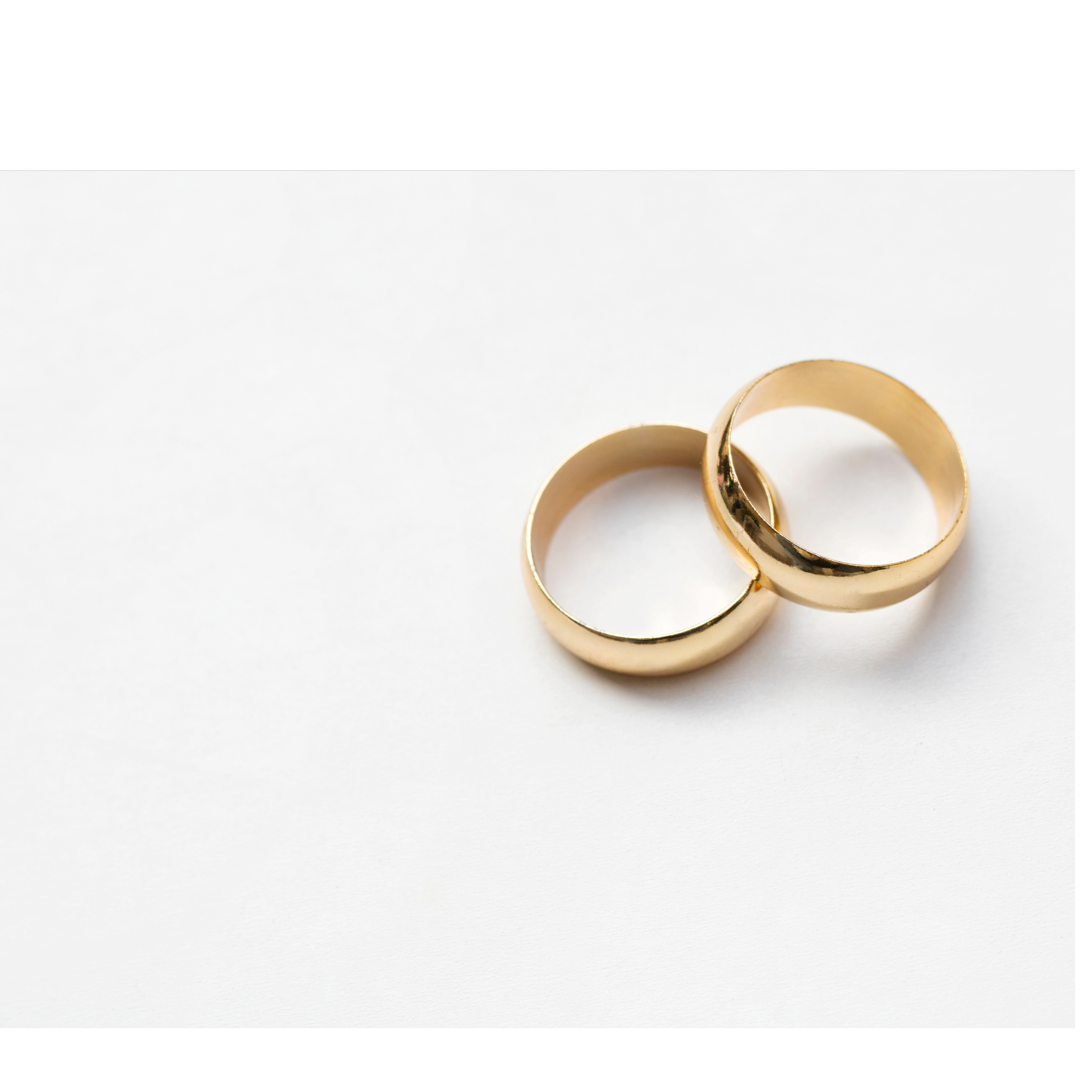Two gold wedding rings resting on a white surface against a white background.