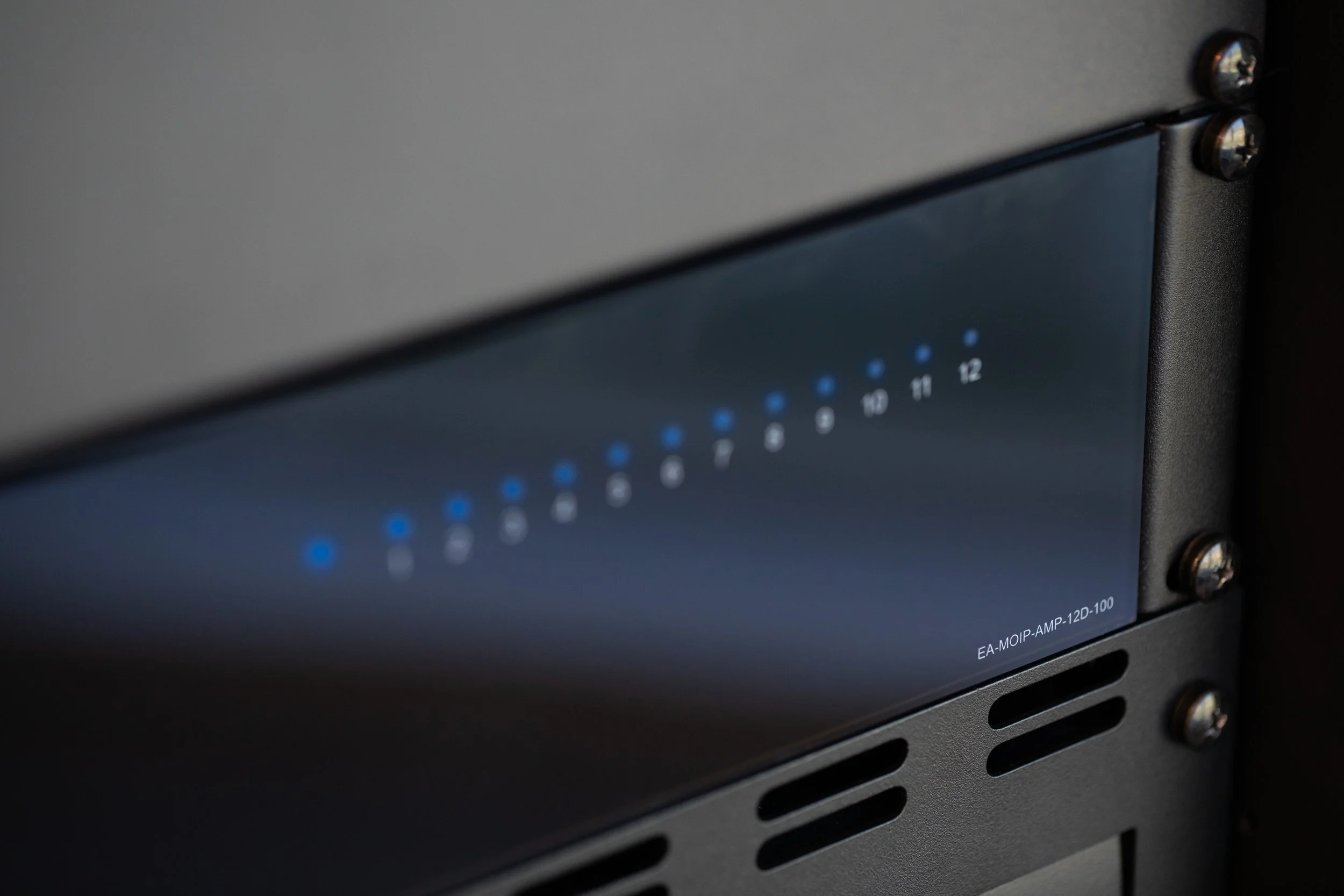 Close-up of a professional audio amplifier or receiver with a black metal casing, silver screws, and a panel displaying blue LED lights and numeric indicators from 1 to 12.