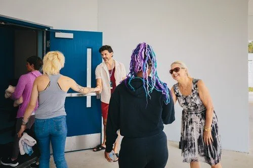 People greeting each other at an entrance, with a blue door and white walls.