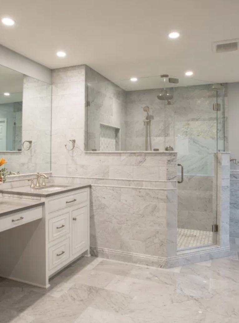 A modern bathroom with marble tiles, a glass-enclosed shower, a white vanity with a marble countertop, and recessed ceiling lights.