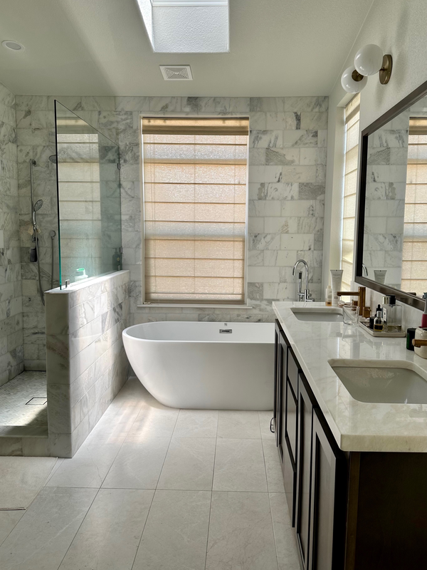 Modern bathroom with marble walls, a freestanding bathtub, a double sink vanity with dark cabinetry, and a shower area with a glass partition.