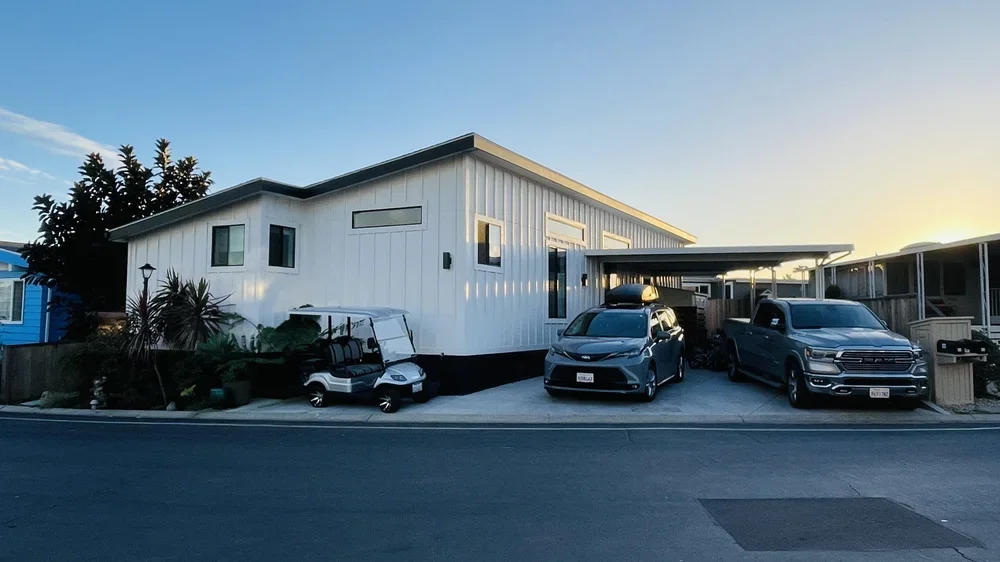 Modern white house with three vehicles parked in front and a small garden with plants and a lamp post on the left side, at sunset.