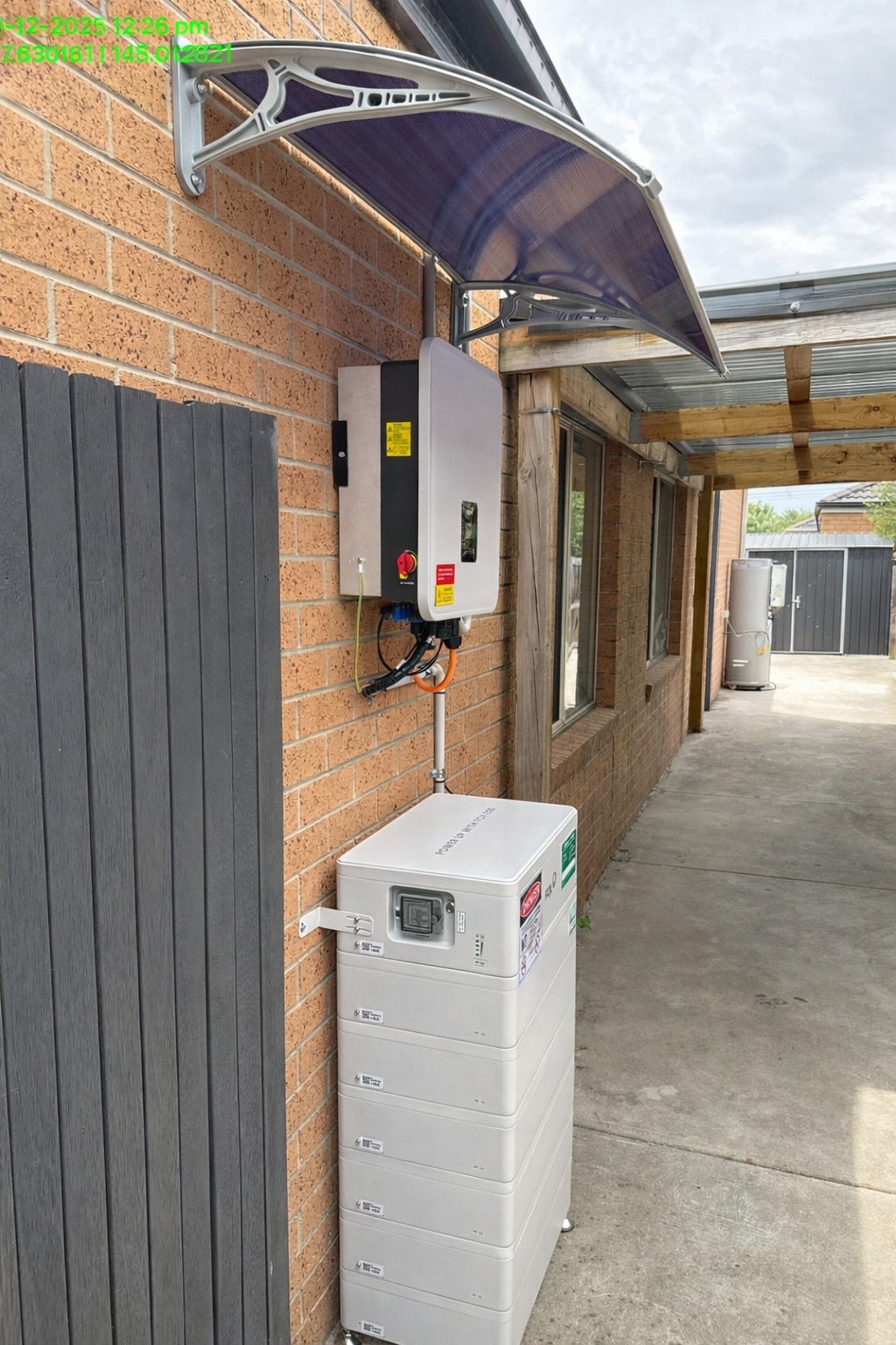 A solar power system with an inverter, battery storage, and a solar panel on a brick wall outside a house.