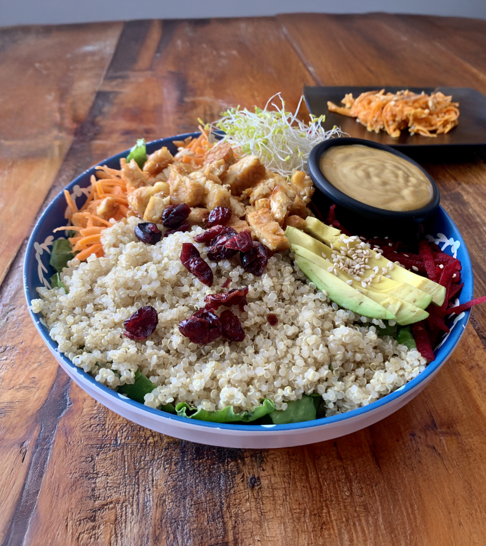 Colorful nourishing bowl with rice, tofu, carrots, avocado, and raisins.