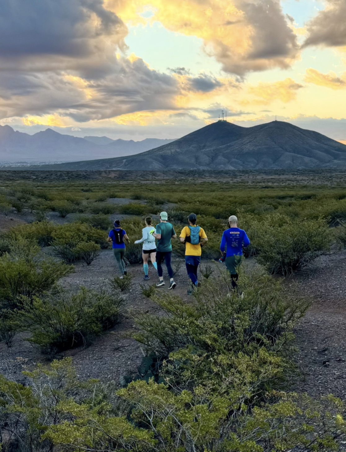 Group of runners on a trail with the Organ Mountains in the distance.