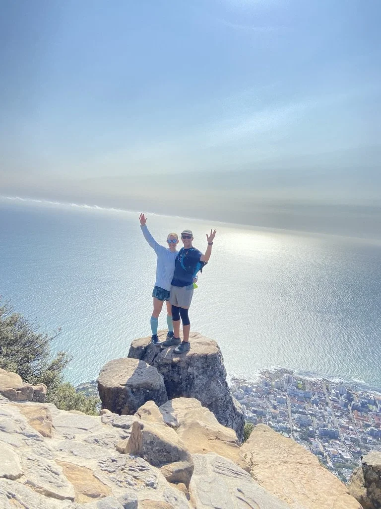 Davena and her partner standing on Lion’s Head with views of Cape Town and the coastline.