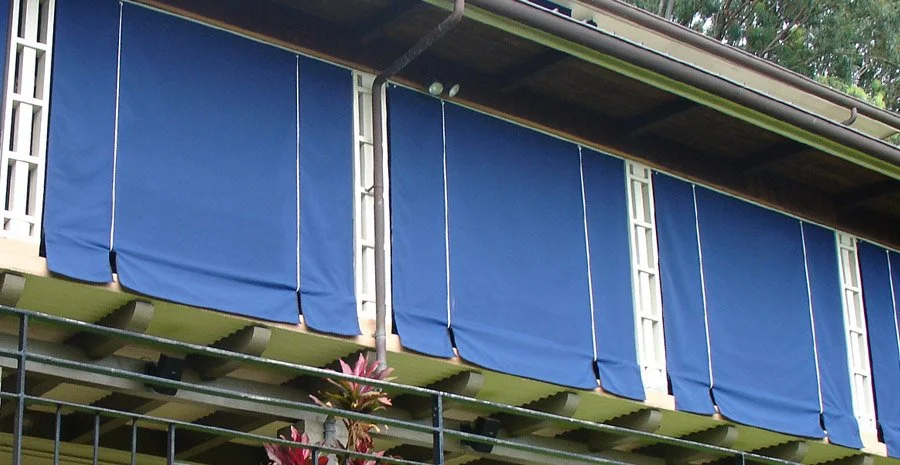 Apartment balcony with blue fabric privacy screens and potted plants below.